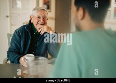 Uomo anziano felice che ha conversazione con il professionista sanitario a casa di cura Foto Stock