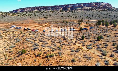 Vista aerea dell'area di parcheggio del deserto e delle scogliere di Mesa. Vista aerea dei veicoli parcheggiati lungo un sentiero polveroso nel deserto con arbusti sparsi e ginepri Foto Stock