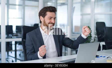 Spensierato uomo d'affari caucasico di mezza età con laptop che balla guardando la macchina fotografica che punta al computer felice scommessa vittoria casinò online vincere Foto Stock