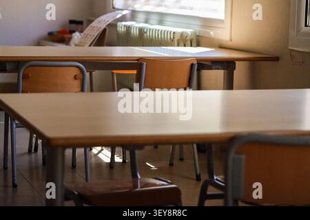 Aula vuota con file di scrivanie e sedie in legno con luce calda alle finestre, radiatore in metallo accanto al pavimento piastrellato, Foto Stock