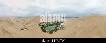 Vista aerea dell'oasi di Huacachina circondata da ampie dune di sabbia, palme e una piccola laguna nel paesaggio desertico di Huacachina, Ica, Perù. Foto Stock