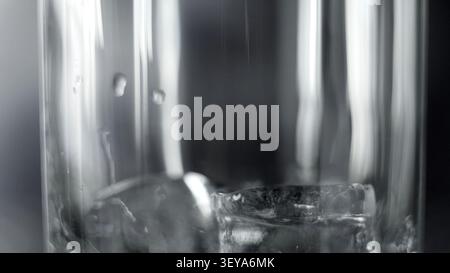Bicchiere d'acqua con cubetti di ghiaccio, condensazione e riflessi, liquido rinfrescante da vicino Foto Stock