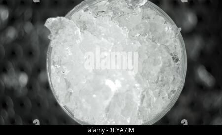 Ghiaccio tritato che riempie un bicchiere trasparente, creando una bevanda fresca con consistenza d'acqua congelata, vista dall'alto Foto Stock