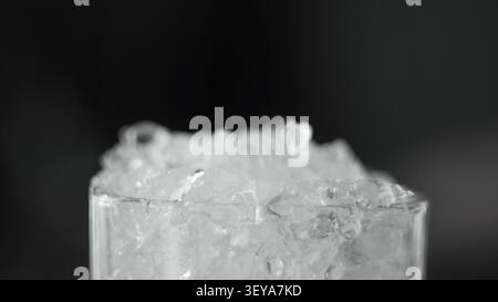 Bicchiere di riempimento per ghiaccio tritato, ingrediente per bevande rinfrescanti fredde, bevande di raffreddamento ad acqua congelate su sfondo scuro Foto Stock