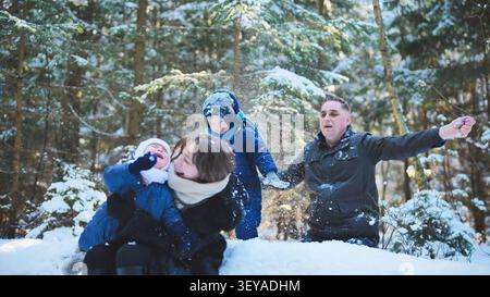 La famiglia gioca insieme nel bosco innevato, i bambini lanciano la neve polverosa e condividono momenti invernali felici Foto Stock