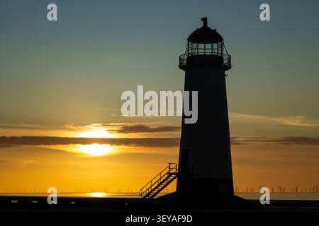 L'impressionante silhouette nera del faro Point of Ayr incorniciata da un vibrante tramonto dorato e arancione su Talacre Beach Foto Stock