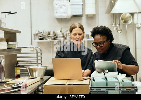 Due chef donne che lavorano insieme su un computer portatile nella cucina del ristorante Foto Stock