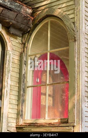 Una vista di una porta a schermo attraverso una finestra ad arco su una casa abbandonata. Foto Stock