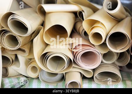 Rotoli di vari tessuti e materiali tessili color crema e beige sono impilati insieme, mostrando diverse trame e motivi, pronti per l'uso in Foto Stock