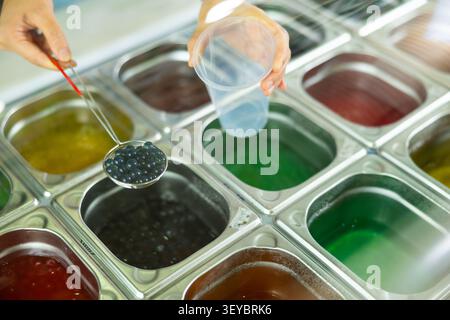 Le mani del barista stanno preparando aggiungendo perle di tè a bolle nere nella tazza Foto Stock