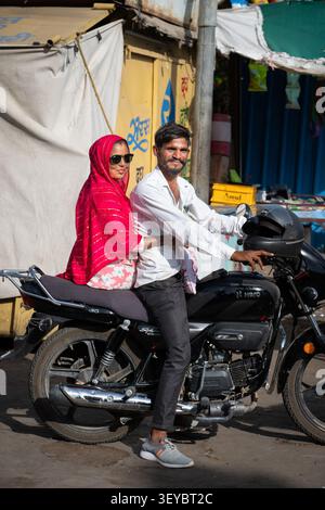 Uomo e donna con un velo rosso e occhiali da sole seduti su una moto al Manak Chowk Market di Jaisalmer, India Foto Stock