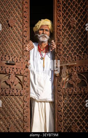 Uomo anziano con turbante giallo in piedi su una porta a Jaisalmer, India Foto Stock