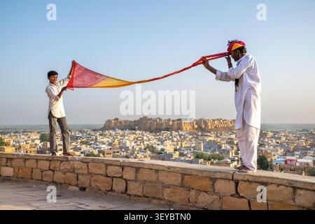 Ragazzo che aiuta suo padre a legare il suo turbante con il Forte di Jaisalmer sullo sfondo, Jaisalmer, Rajasthan, India Foto Stock
