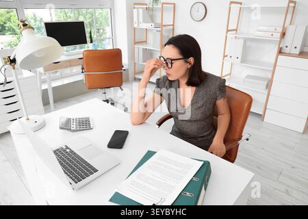 Donna d'affari stressata seduta alla scrivania in un ufficio moderno Foto Stock