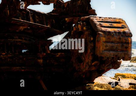 Vista ravvicinata di strutture metalliche corrose dagli agenti atmosferici da una nave sommersa che poggia su un paesaggio costiero Foto Stock