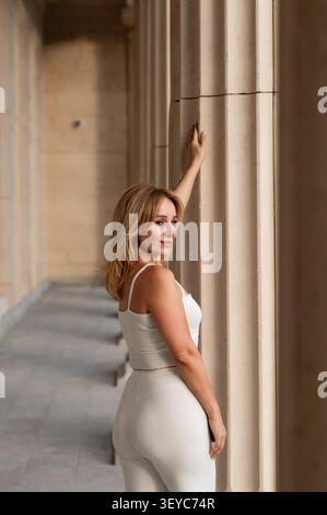 Woman White outfit Columns Architecture - Una donna con un abito bianco si appoggia contro una colonna in un ambiente architettonico. Foto Stock