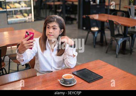 Ritratto di uno stile di vita moderno di una donna d'affari transgender isana del sud-est asiatico, che ha compiuto 40 anni, scattando selfie e posando in un tavolino. Questo com. Orizzontale Foto Stock