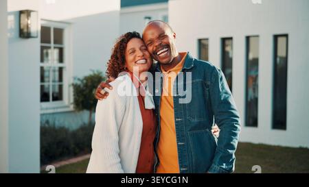 Ridi, abbraccia e coppia con una nuova casa, cura e supporto con un partner maturo per gli investimenti immobiliari. Uomo, donna e abbraccio africani per gli immobili Foto Stock
