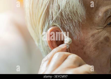 Primo piano di un anziano dai capelli grigi che usa il suo apparecchio acustico nell'orecchio con spazio di copia. Concetto di perdita dell'udito e problemi all'orecchio. Foto Stock