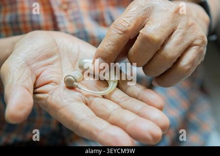 Paziente anziano che tiene in mano un apparecchio acustico. Apparecchio acustico medico su uomo anziano. Primo piano. Medicina, perdita dell'udito, concetto di trattamento Foto Stock
