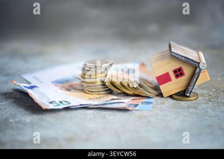 Il finanziamento è fallito, il modello di casa è crollato con una pila di monete e banconote, concetto di capitale proprio troppo basso, debito eccessivo o tassi di interesse in aumento, Foto Stock