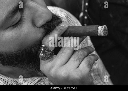 Primo piano ritratto in bianco e nero di un uomo barbuto che fuma un sigaro, evidenziando un dettagliato anello cranico d'argento sulla sua mano. Foto Stock