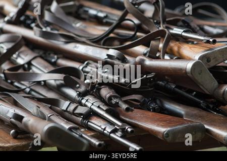 Primo piano di una grande pila di vecchi fucili militari in legno e cinturini in pelle. Armi storiche dell'esercito impilate una sopra l'altra. Foto Stock