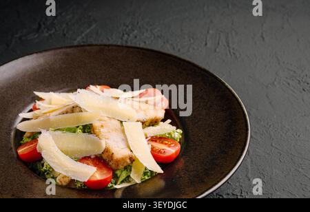 Un piatto ben organizzato presenta pollo alla griglia su un letto di verdure fresche e pomodori ciliegini, condito con sottili fette di formaggio, per un pasto leggero e salutare. Foto Stock