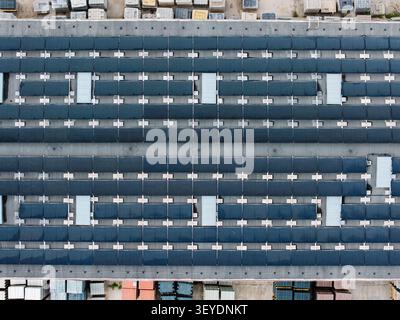 Vista aerea del tetto di una fabbrica di pavimentazione in pietra con ampi pannelli solari e pile di materiali per pavimentazione nel cortile sottostante a riga, Lettonia. Foto Stock