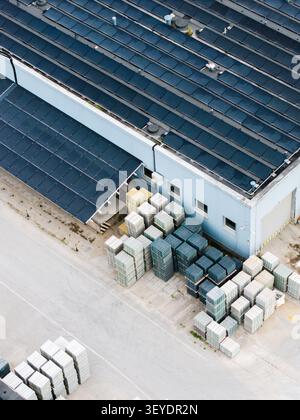 Veduta aerea di una fabbrica di lastre di pavimentazione con pannelli solari sul tetto e pile organizzate di lastricatrici di calcestruzzo nel cantiere industriale di riga, Latvi Foto Stock