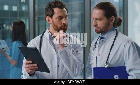 Due concentrati Caucasico con esperienza due uomini medici parlare navigare tablet digitale app chirurghi medici parlare di cure mediche trattamento farmacologico Foto Stock