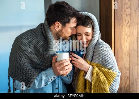 Una coppia amorevole condivide una tranquilla mattinata d'inverno avvolta da coperte calde, trovando intimità emotiva Foto Stock
