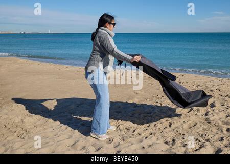 Donna che prepara un posto per picnic spargendo una coperta su una spiaggia soleggiata. Foto Stock