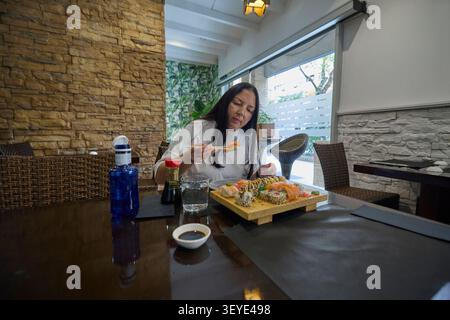 Primo piano di una donna che mangia sushi di salmone con bacchette in un ristorante. Foto Stock