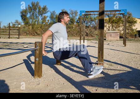 L'uomo che esegue il tricep si immerge sulle barre di metallo durante l'allenamento all'aperto. Foto Stock