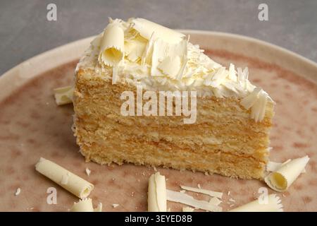Fetta di torta in spugna ricoperta di ricci di cioccolato bianco su un piatto di ceramica Foto Stock