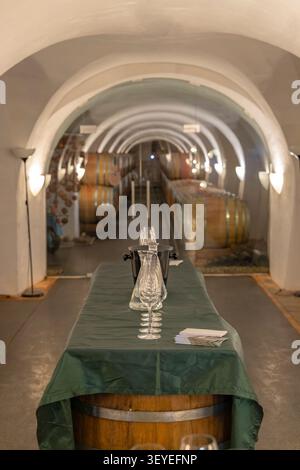 Bicchieri da vino e un refrigeratore su un tavolo in botte pronti per la degustazione in una cantina ad arco Foto Stock