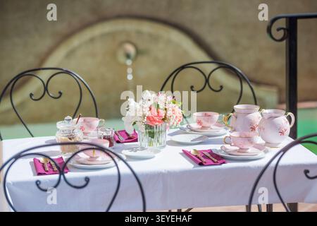 Tazze da tè, un centrotavola floreale e allestimenti disposti su una tovaglia bianca per cene all'aperto Foto Stock