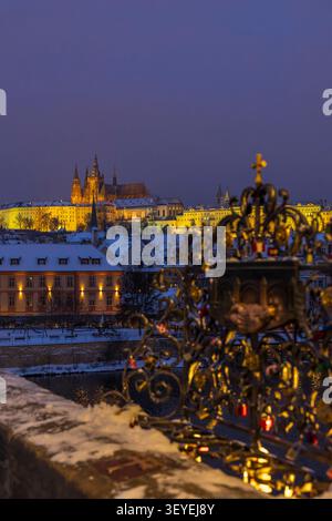 Castello di Praga illuminato e paesaggio urbano visto da Karluv Most con ringhiere d'amore in inverno Foto Stock