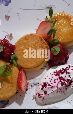 Frittelle dorate con panna montata, fragole, salsa di bacche e menta su un piatto a motivi geometrici Foto Stock