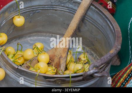 Ciliegie dolci gialle fresche in una tradizionale pentola in metallo con un cucchiaio di legno, che illustra la preparazione fatta in casa delle conserve, la cucina rustica e il mare Foto Stock