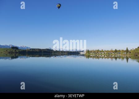 A hot air balloon floats over a lake with mountains in the background in a clear atmosphere, Lech Reservoir, Hochplatte with Ammergebirge, Tegelberg, Foto Stock