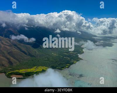 Una prospettiva aerea di Molokai orientale rivela un drammatico contrasto tra le montagne coperte di nuvole e la costa illuminata dal sole che incontra il blu profondo del Pacifico - Molo Foto Stock