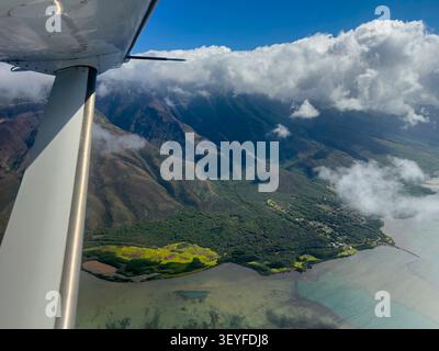 Una prospettiva aerea di Molokai orientale rivela un drammatico contrasto tra le montagne coperte di nuvole e la costa illuminata dal sole che incontra il blu profondo del Pacifico - Molo Foto Stock