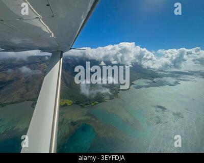 Una prospettiva aerea di Molokai orientale rivela un drammatico contrasto tra le montagne coperte di nuvole e la costa illuminata dal sole che incontra il blu profondo del Pacifico - Molo Foto Stock