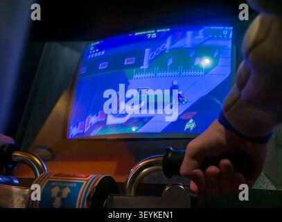 Visitatore che gioca al classico videogioco arcade Paperboy su una macchina arcade originale durante un evento di gioco rétro. Foto Stock
