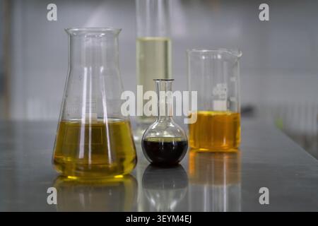 Vetreria da laboratorio contenente liquidi di diversi colori disposti su una superficie di lavoro in acciaio inox. L'immagine raffigura un ambiente di laboratorio funzionante Foto Stock