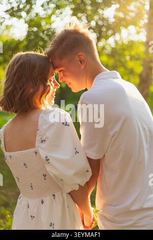 Una coppia romantica con la fronte toccata e le mani strette gode di un pomeriggio caldo e soleggiato in un parco Foto Stock