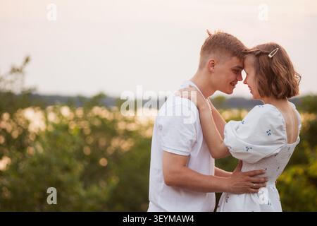 Un momento romantico condiviso tra un giovane uomo e una donna, con la fronte che si toccano in un abbraccio amorevole tra il delicato bagliore della natura Foto Stock