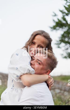 Una giovane coppia gioiosa condivide un momento tenero all'aperto, i loro volti si illuminano di felicità e amore Foto Stock